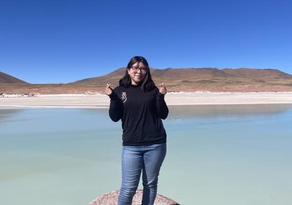 Michelle Lamadrid Benavides standing in front of a lake making finger hearts. 